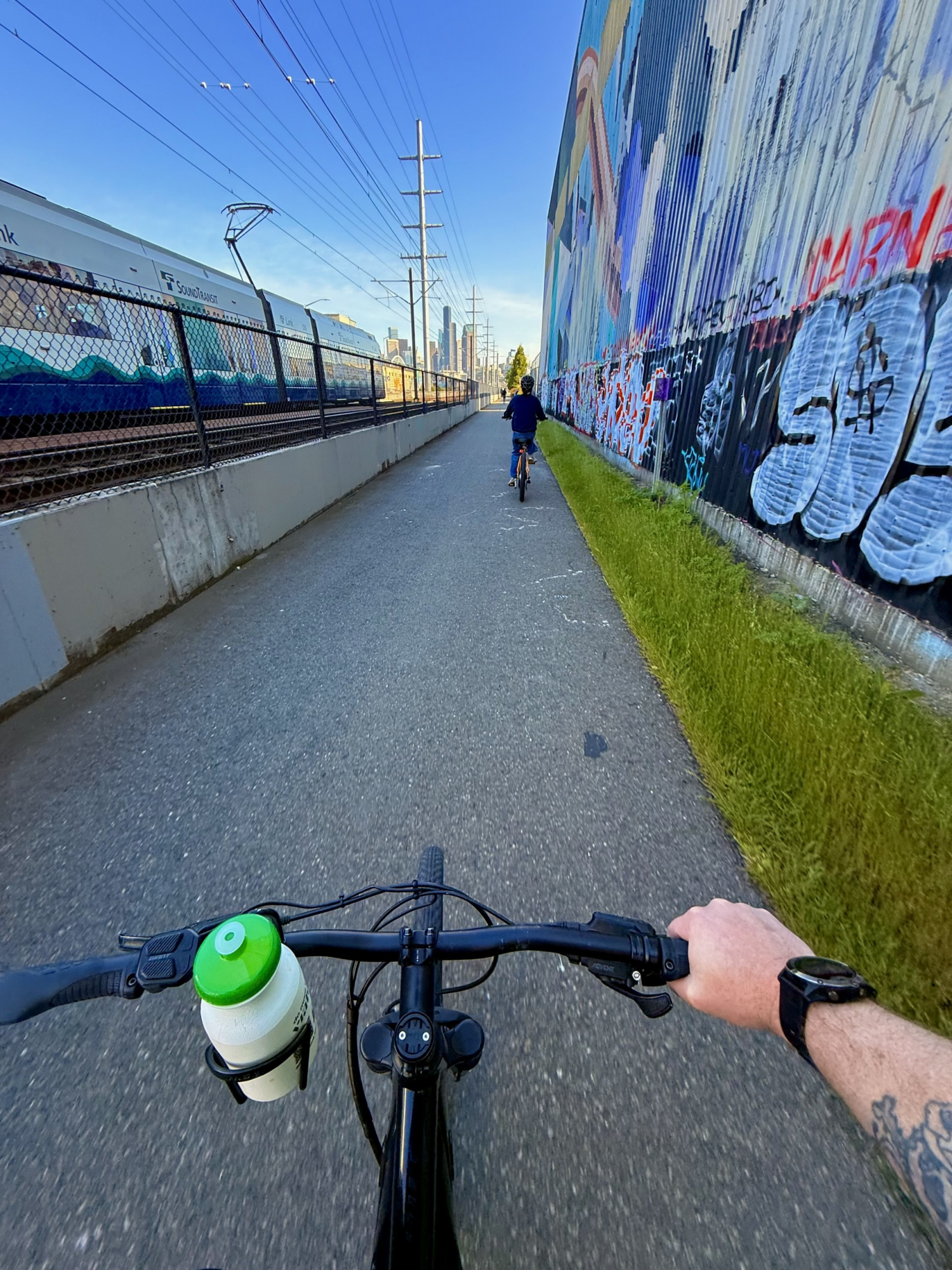 Cyclist's view riding beside graffiti-covered wall and train on parallel tracks.
