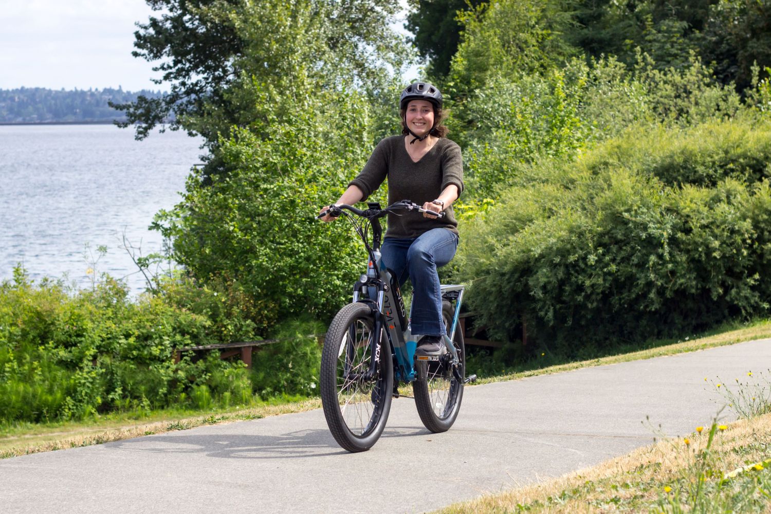 Person riding a bicycle on a path near water and trees.